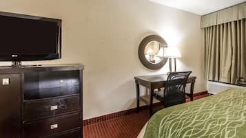 Quarto de hotel com cama, escrivaninha com cadeira, televisão em um móvel, espelho e luminária.