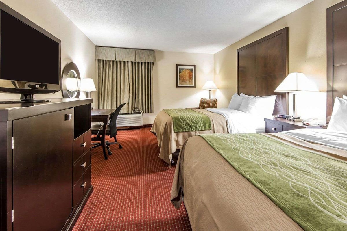 A hotel room with a bed, a desk, a chair, a TV, and a wardrobe.
