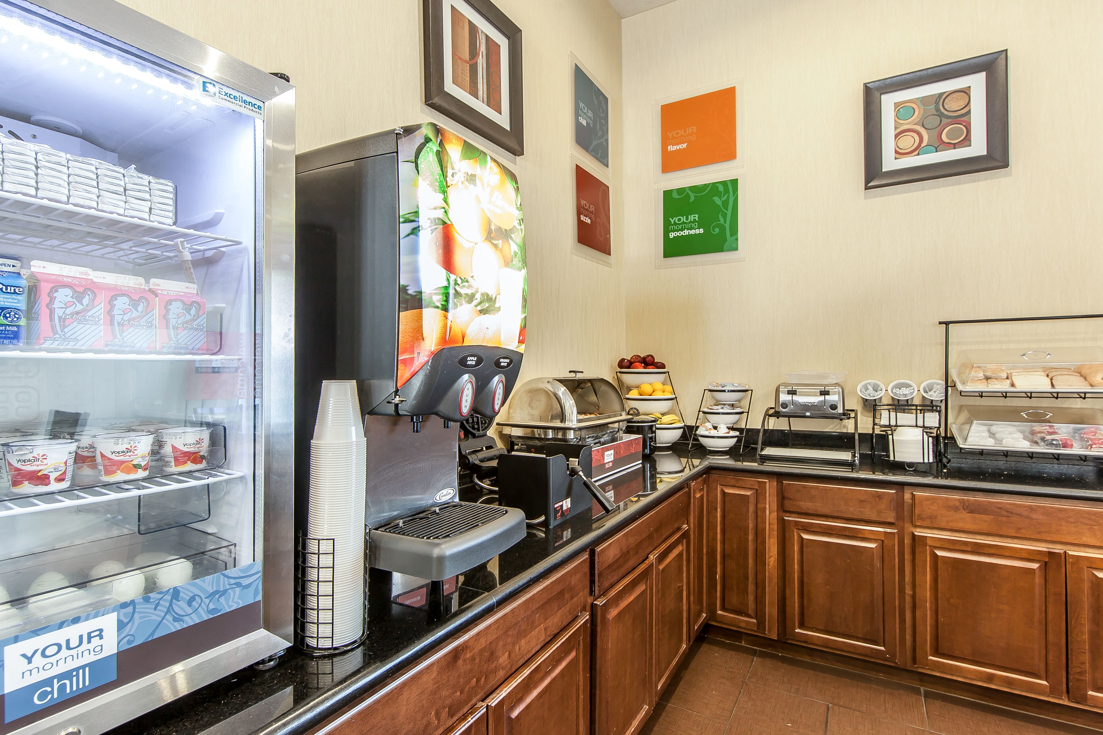 A breakfast bar with a coffee machine, a refrigerator with yogurt and juice, and a fruit display.