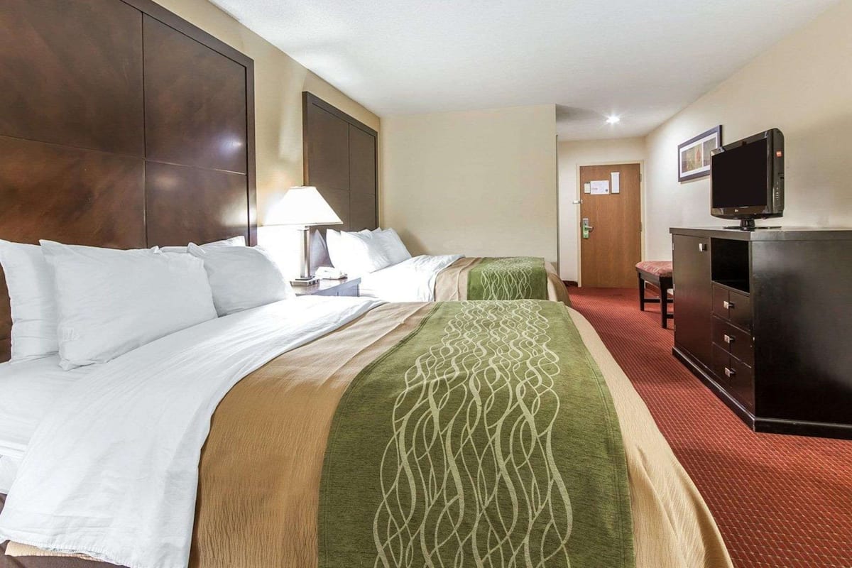 A hotel room with two beds, a TV, a desk, and a lamp.