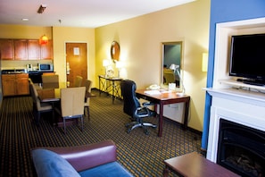Une chambre d’hôtel comprenant un canapé, une table à manger avec des chaises, un coin cuisine, une télévision et une cheminée.