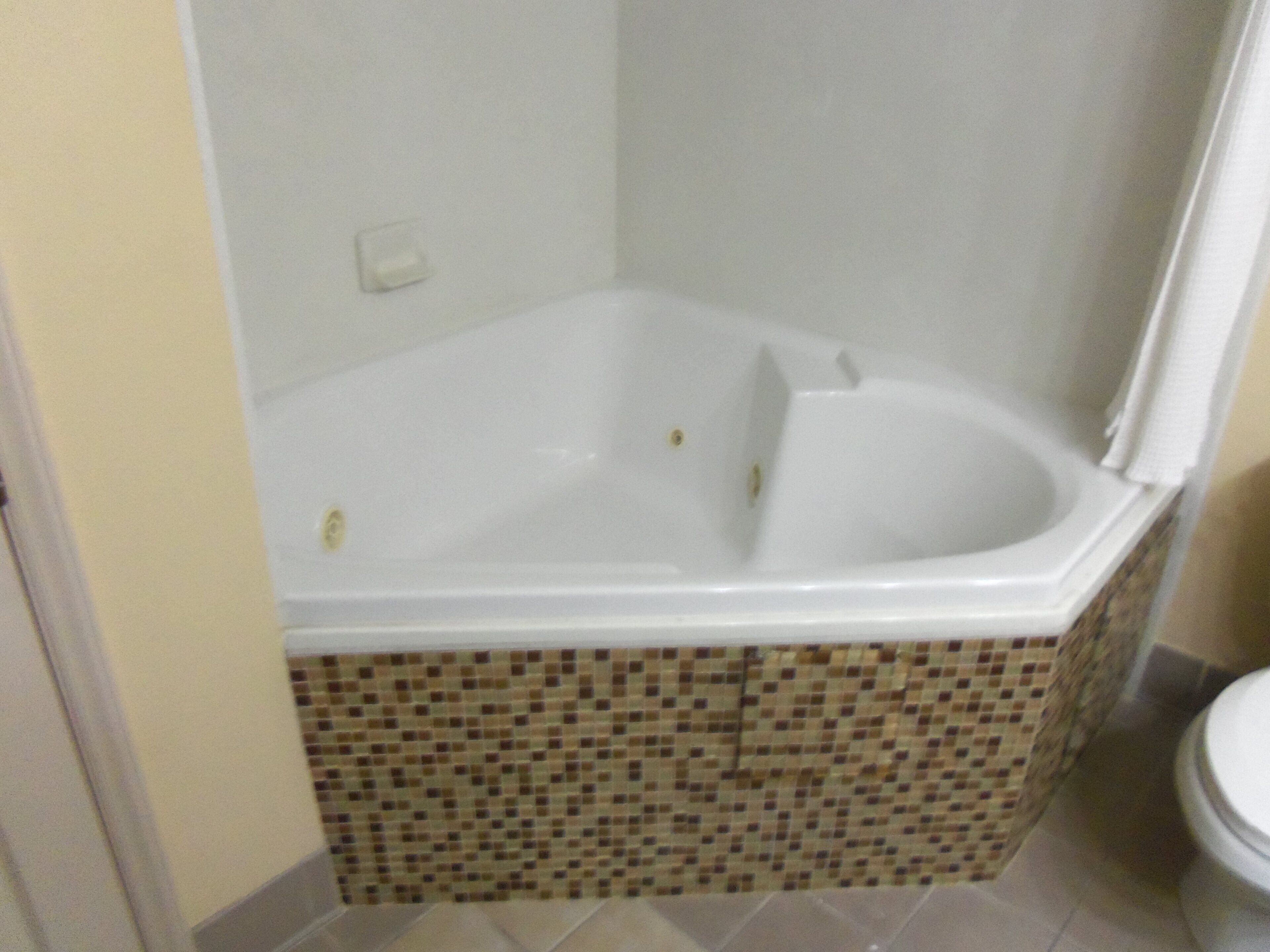 Une salle de bain avec une baignoire d’angle, des murs carrelés et des toilettes.
