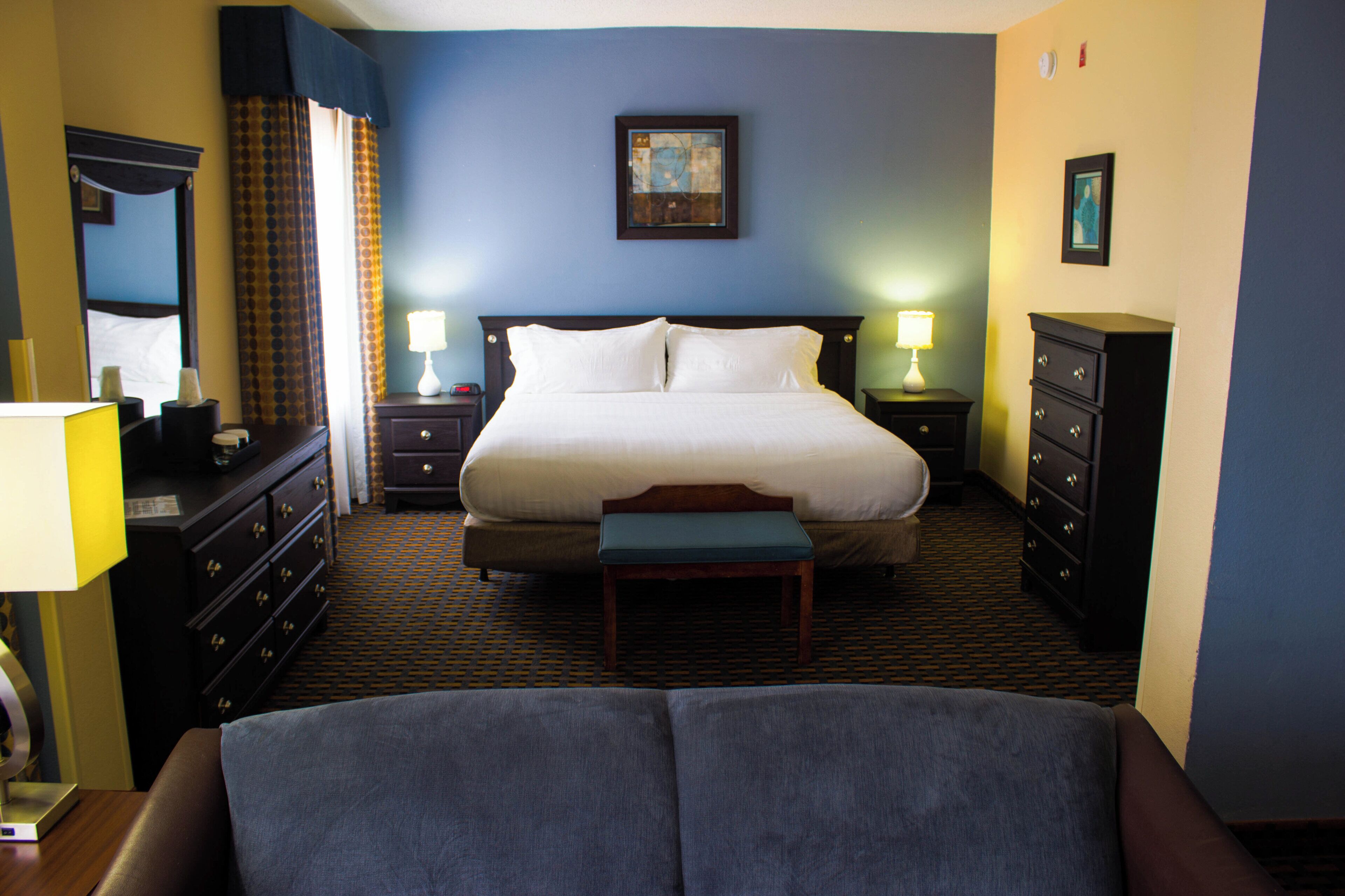 Une chambre d’hôtel avec un grand lit, deux tables de chevet, une commode, un banc et un miroir.