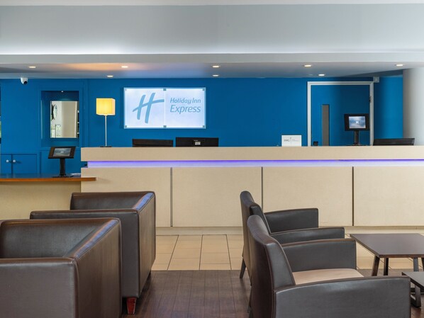 A Holiday Inn Express lobby with a reception desk, seating area, and a large screen displaying the hotel name. - Holiday Inn Express London - Greenwich by IHG (London)
