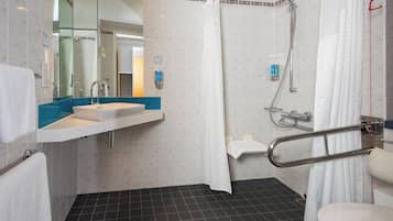 A bathroom with a white sink, mirror, and a shower area with a grab bar.
