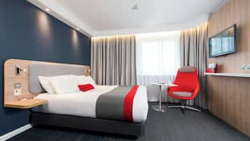 A hotel room with a bed, bedside table, chair, TV, and curtains.