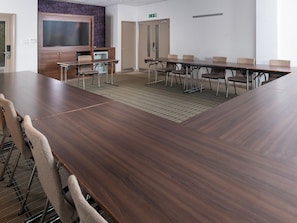 Un salón de conferencias con una gran mesa de madera, varias sillas, un televisor y un papel tapiz estampado.