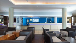 A modern hotel lobby with a reception desk, seating area, and a blue accent wall. - Holiday Inn Express London - Greenwich by IHG (London)