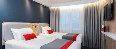 Een hotelkamer met twee bedden, een flatscreen televisie, een raam met gordijnen en een houten wand.