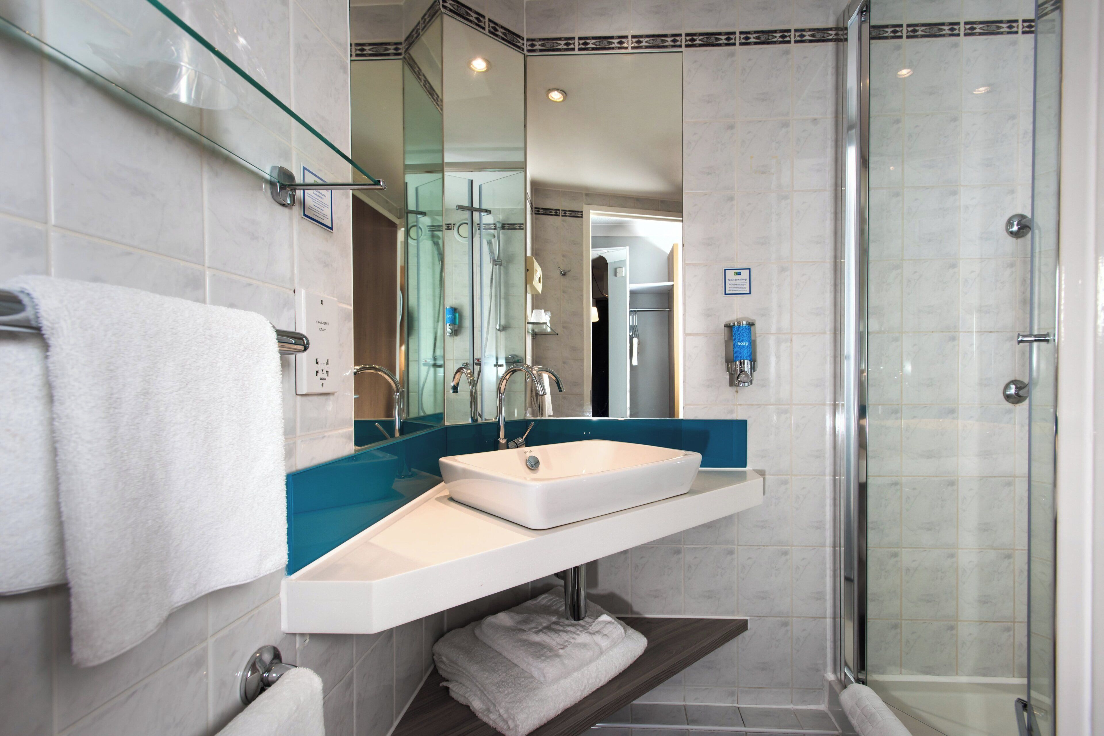 A modern bathroom with a glass shower enclosure, a white sink, and a blue accent wall.
