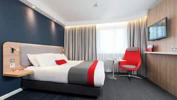 A hotel room with a bed, bedside table, chair, TV, and curtains.