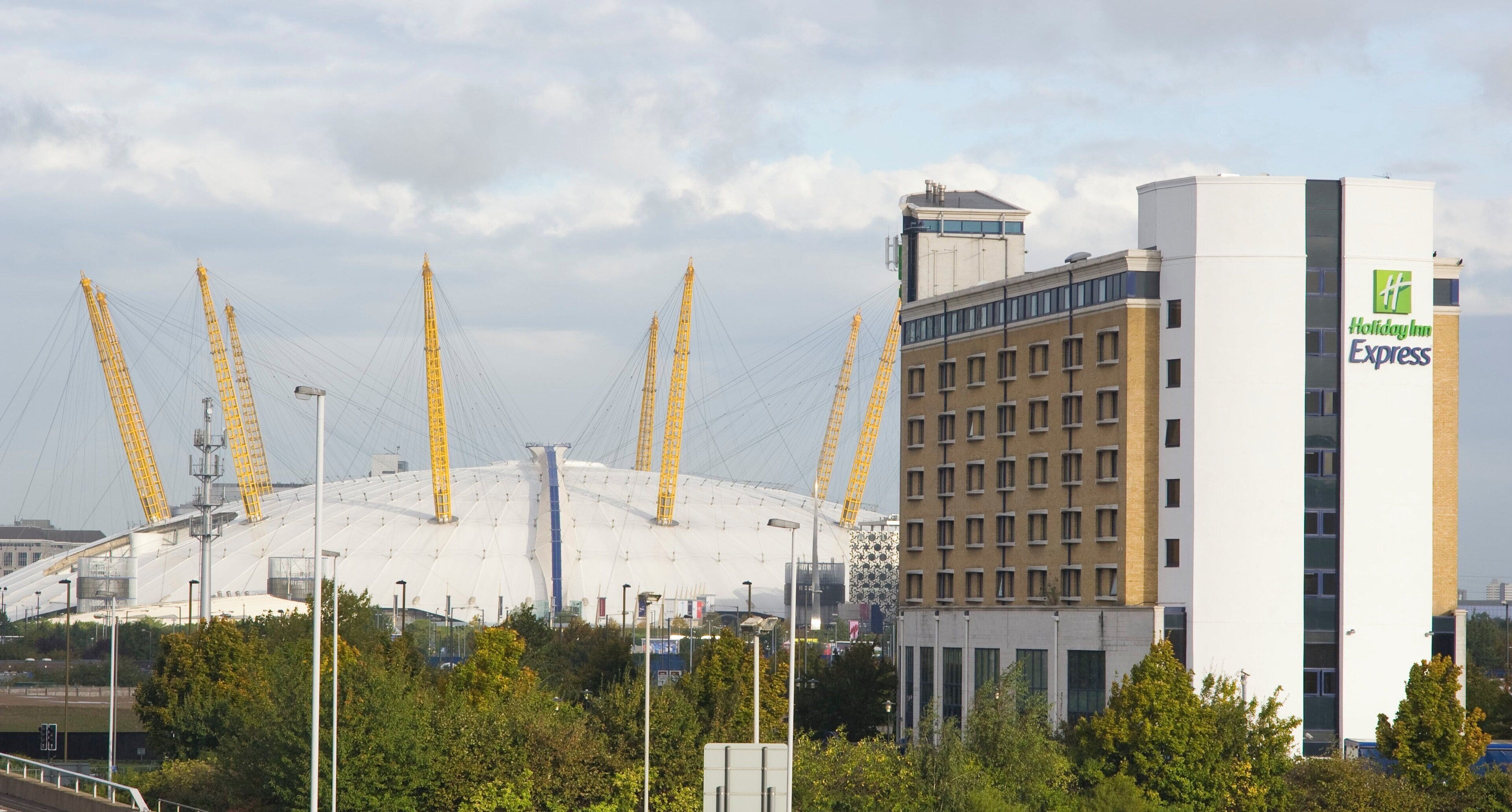 A Holiday Inn Express hotel with a modern design, featuring a prominent white building and a large stadium-like structure with cranes in the background.