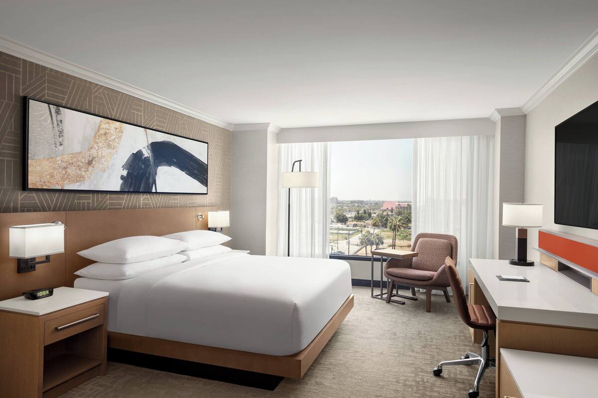 A hotel room with a large bed, a desk, a chair, a TV, and a window with a view.