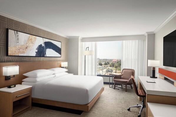A hotel room with a large bed, a desk, a chair, a TV, and a window with a view.