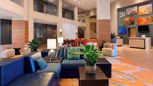 A spacious lobby with a high ceiling, multiple seating areas, a reception desk, and artwork on the walls.