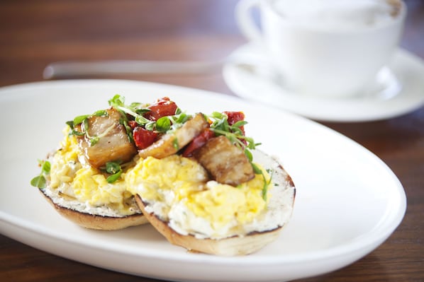 A breakfast plate with eggs, bacon, and greens on a white plate.