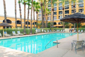 A pool area with lounge chairs and umbrellas, surrounded by palm trees and a building with balconies. - Delta Hotels by Marriott Anaheim Garden Grove (Garden Grove)