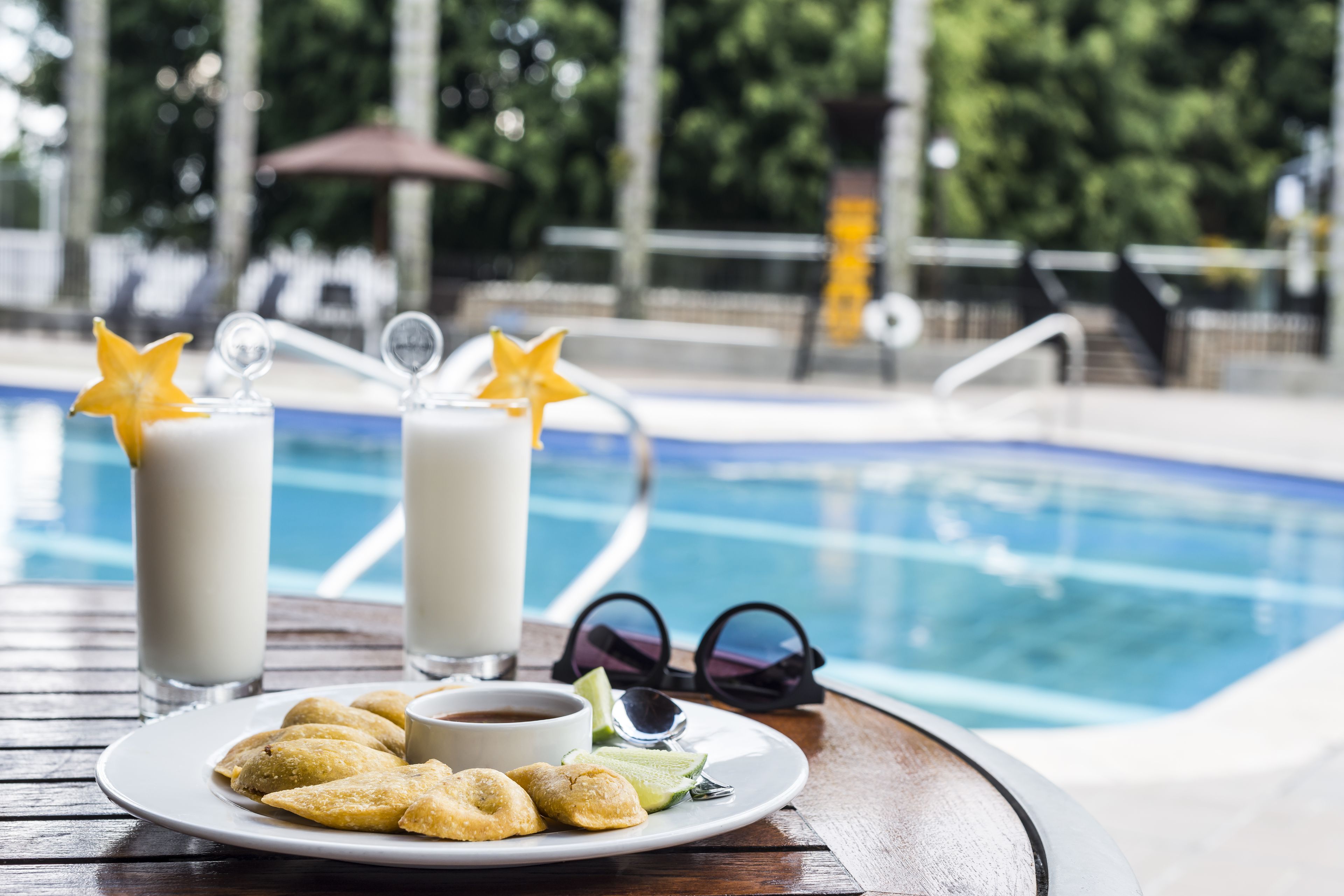 Una mesa de comedor con un plato de pasteles, dos vasos de una bebida cremosa con adornos en forma de estrella, una taza de café y un par de gafas de sol.