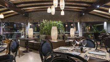 A restaurant with high ceilings, woven light fixtures, and a central seating area surrounded by tables and chairs.
