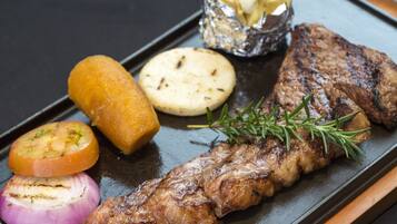 Un filete acompañado de verduras a la parrilla y un recipiente pequeño con mantequilla sobre un plato negro.