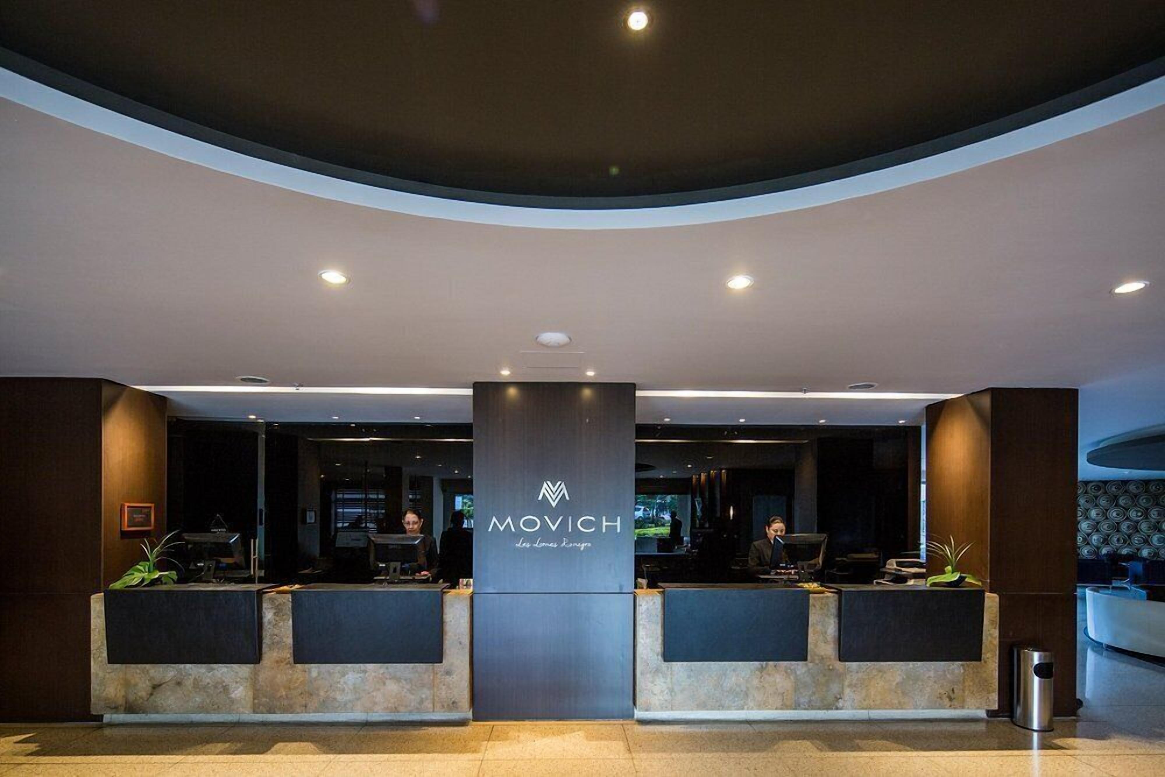 A reception area with a modern design, featuring a central pillar with the logo 'MOVICH' and two reception desks.