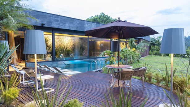 A modern outdoor pool area with a wooden deck, lounge chairs, and a table with umbrellas.
