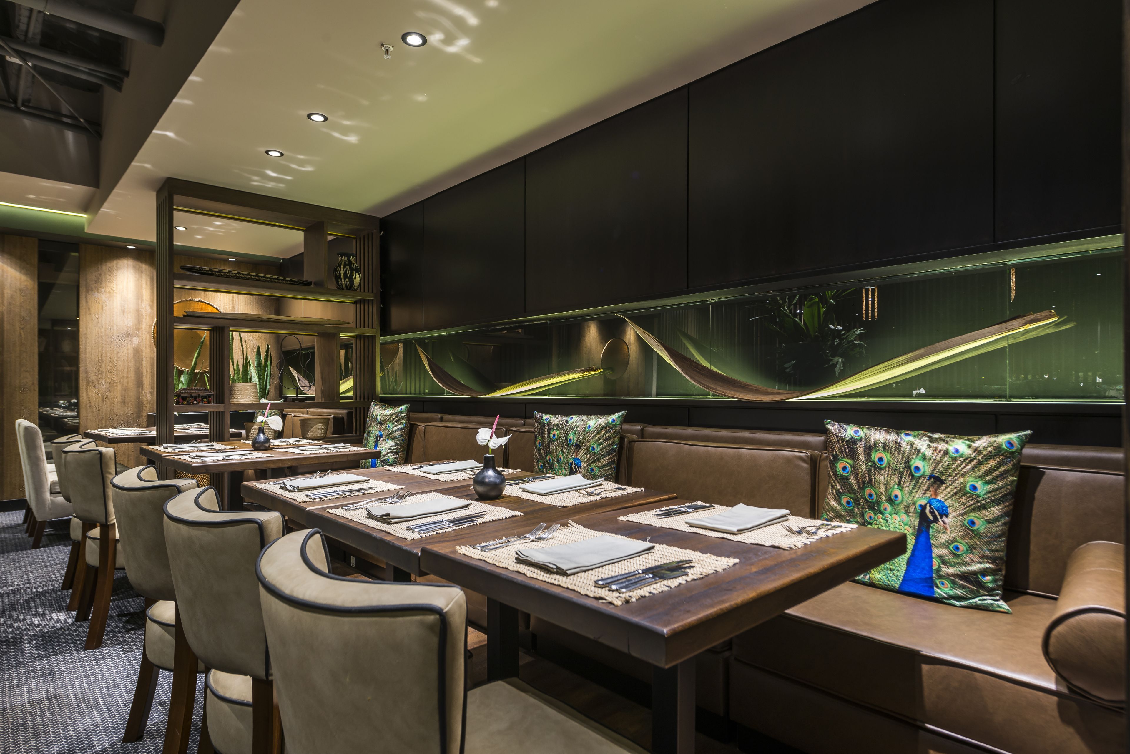 A modern dining area with long tables, cushioned seating, and a large aquarium wall.