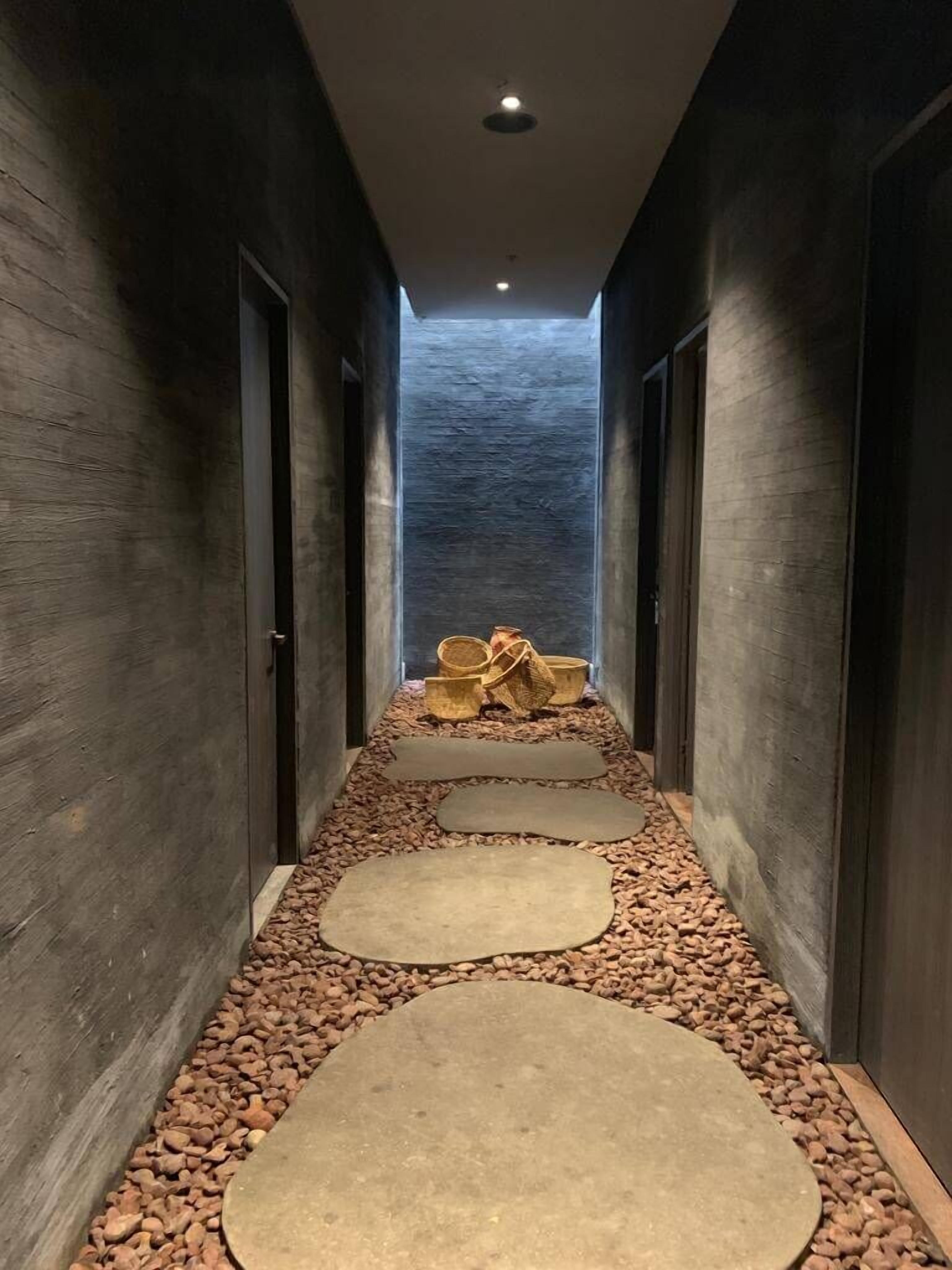 A narrow hallway with wooden walls and a pebble-tiled floor, leading to a room with a large window and a view of the water.