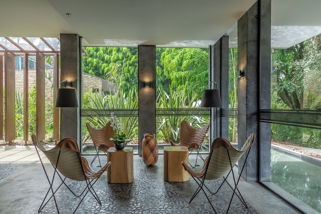 A modern outdoor seating area with chairs and tables, large windows with a view of greenery, and a stone floor.