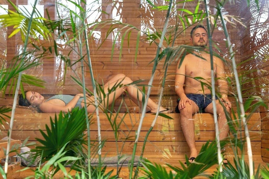 Two people in wooden tubs with plants around them.