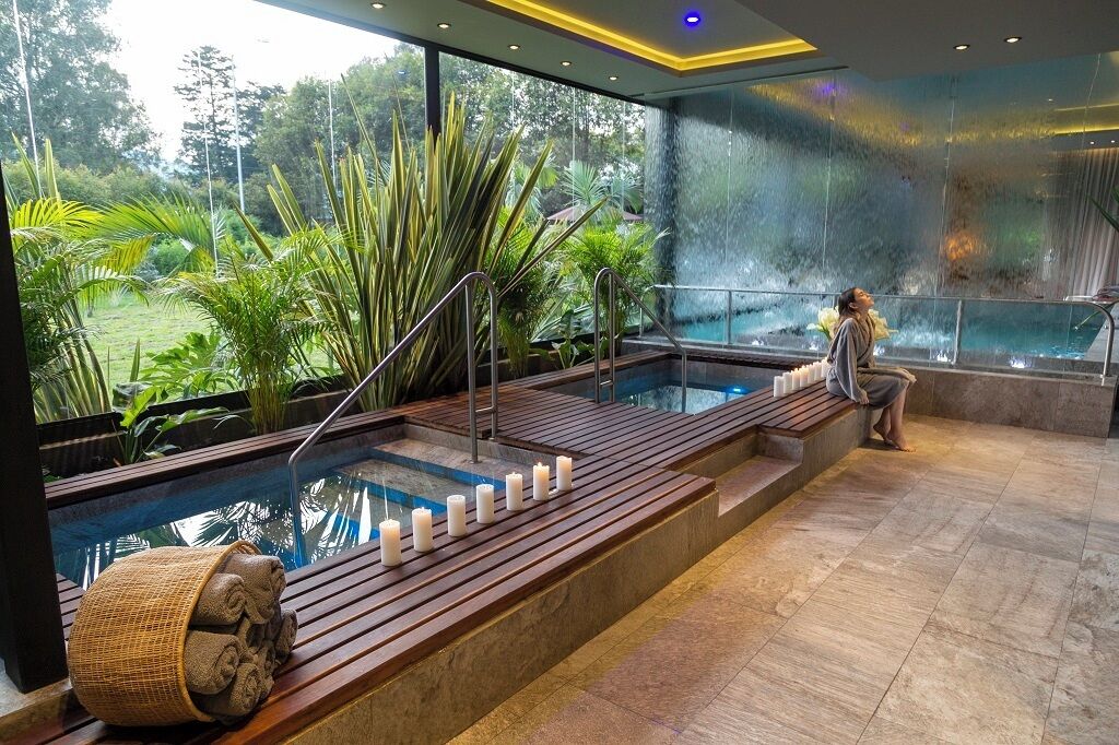 A spa area with a pool, wooden benches, and a waterfall feature.