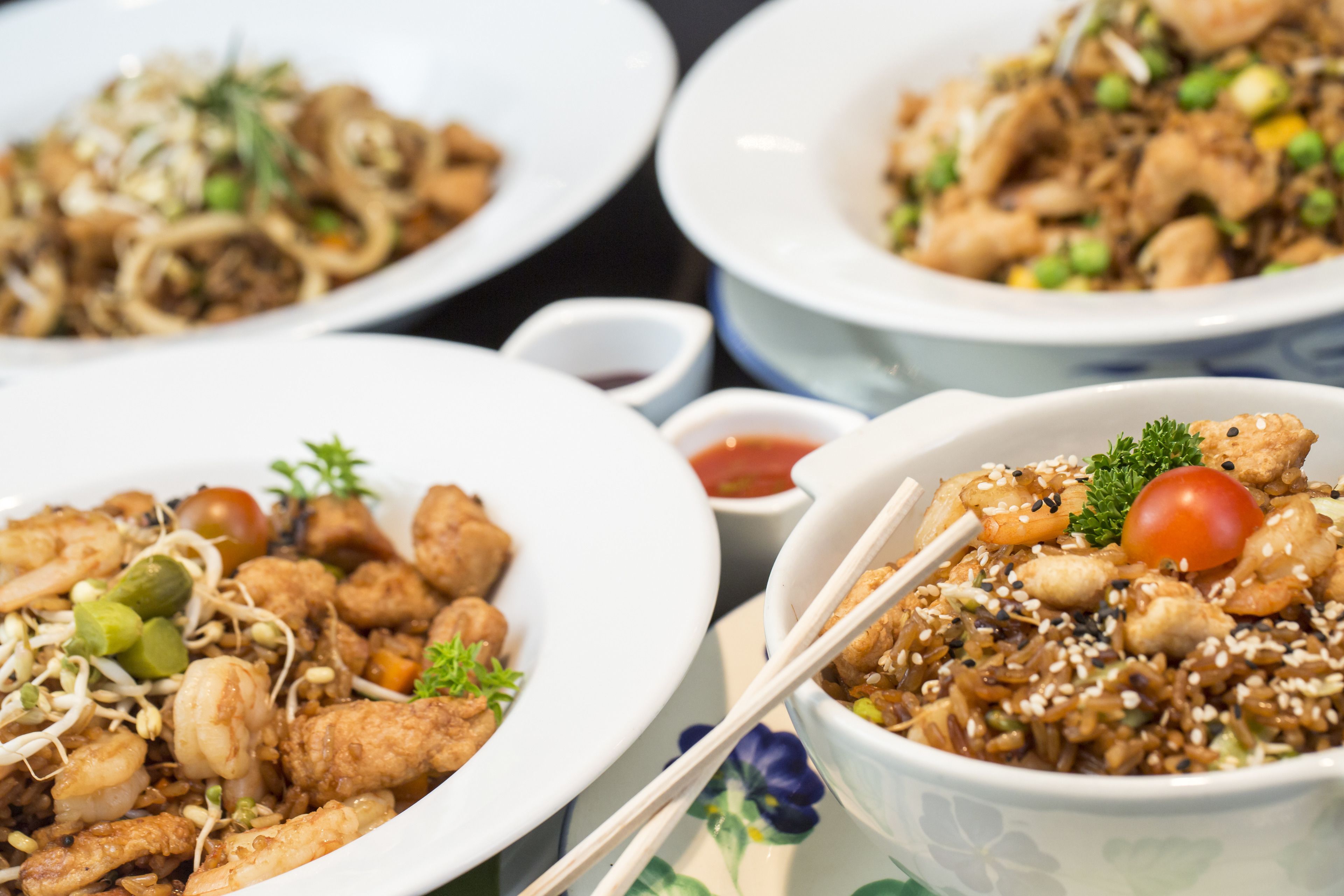 Three plates of stir-fried dishes with various vegetables and shrimp, served on white plates with chopsticks.