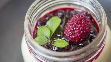 A close-up of a jar with a raspberry and leaves on top.