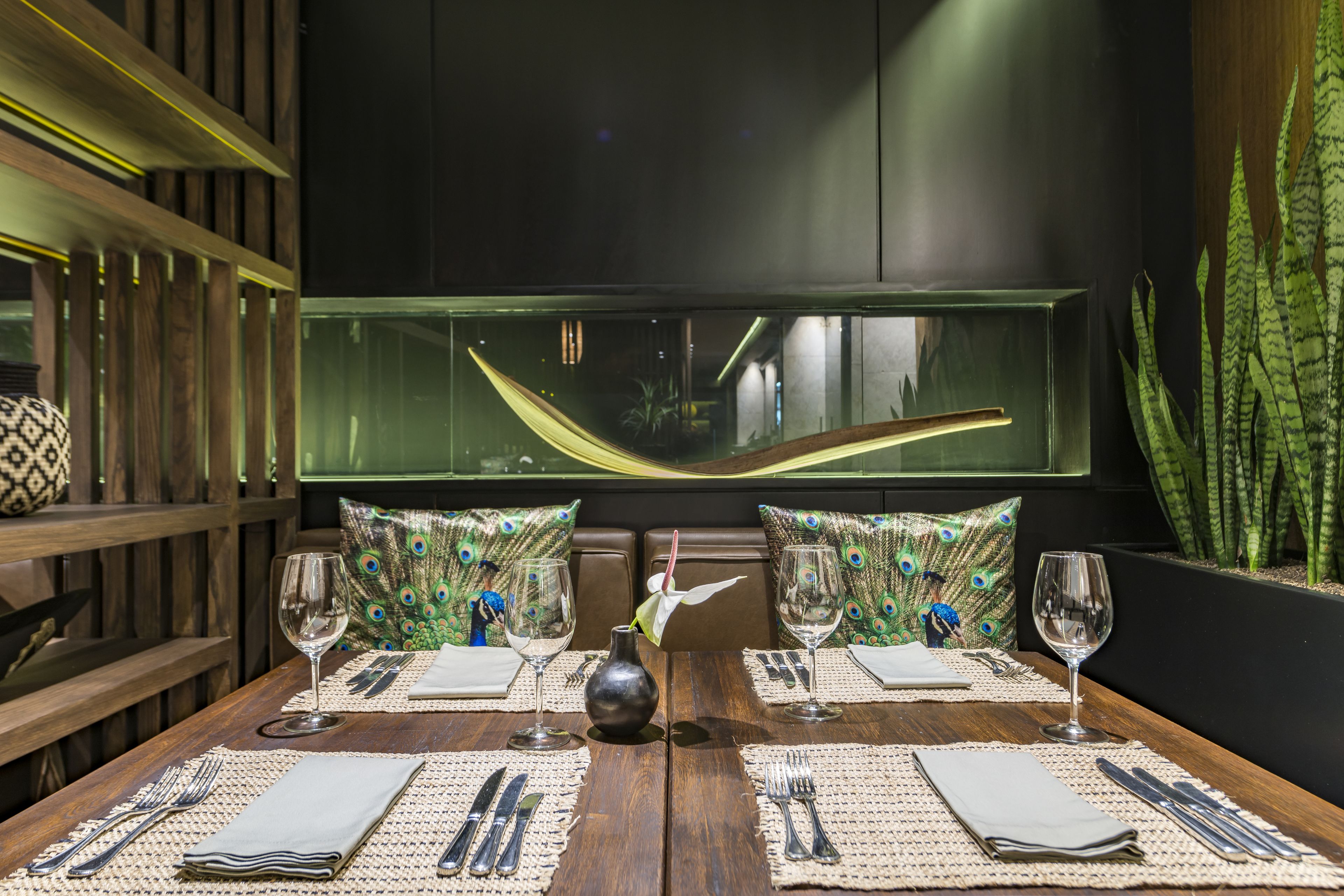 Una mesa de comedor dispuesta con un jarrón, dos almohadones de pavo real y un cojín con motivos de pavo real.