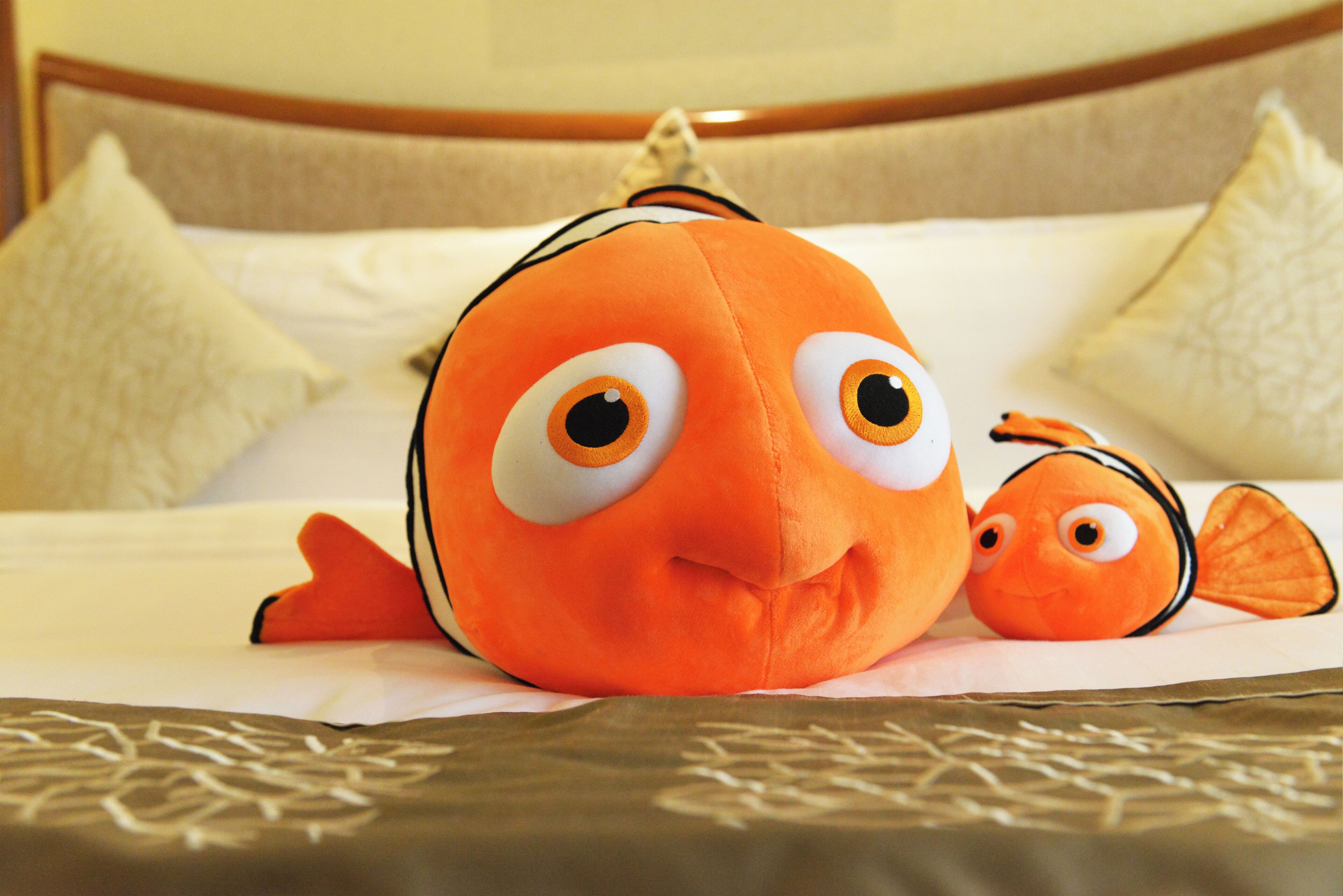 Un peluche con forma de pez sobre una cama con almohadas y cabecero.