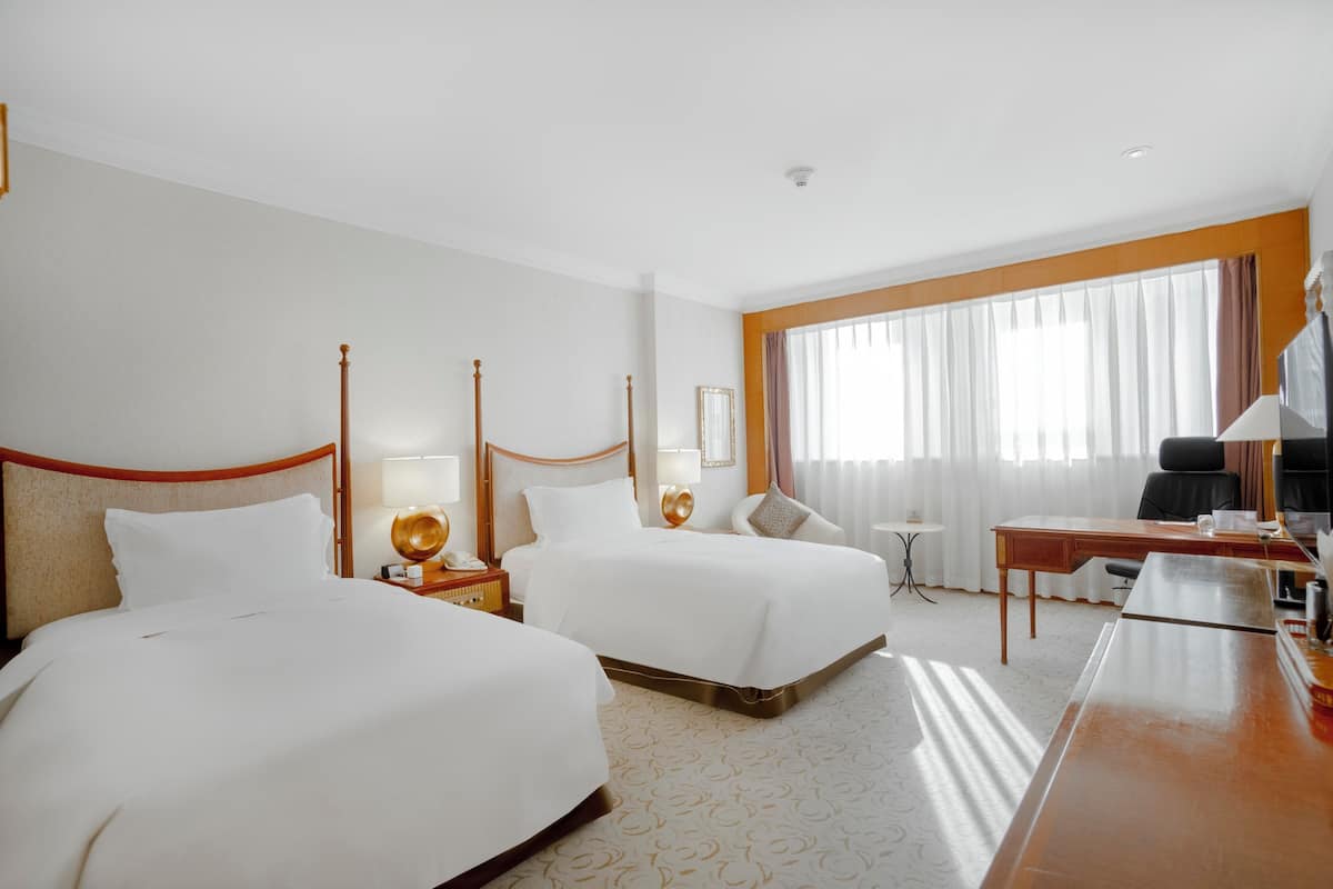 Een hotelkamer met twee bedden, een bureau, een stoel, een tafeltje en een raam met gordijnen.