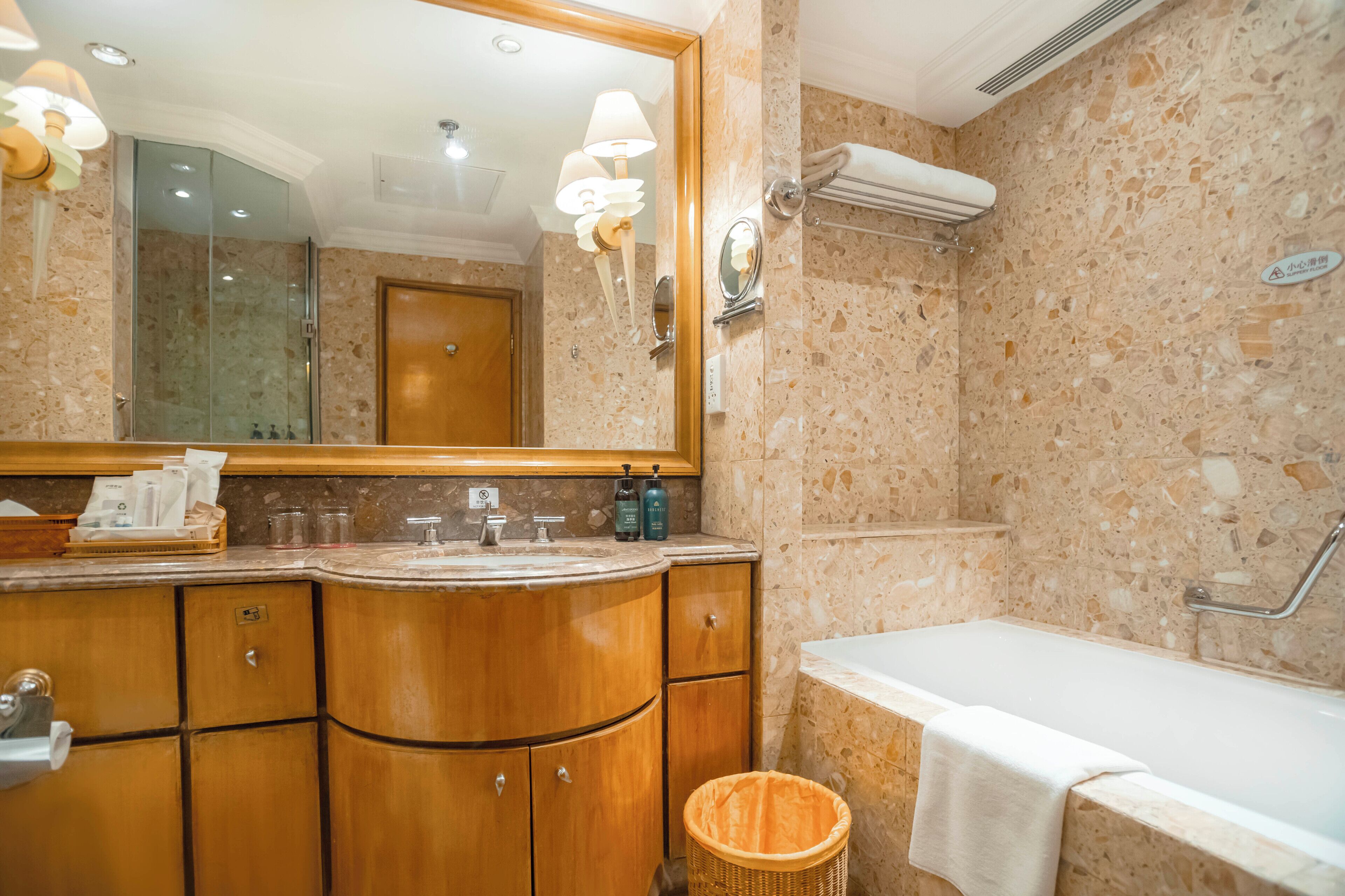 A bathroom with a marble wall, wooden vanity, a large mirror, and a bathtub.
