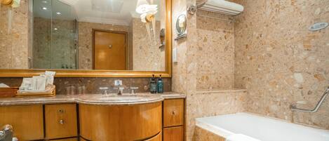 A bathroom with a marble wall, wooden vanity, a large mirror, and a bathtub.