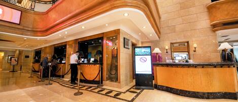 A hotel reception area with a marble floor, a reception desk, a digital information kiosk, and a staircase.