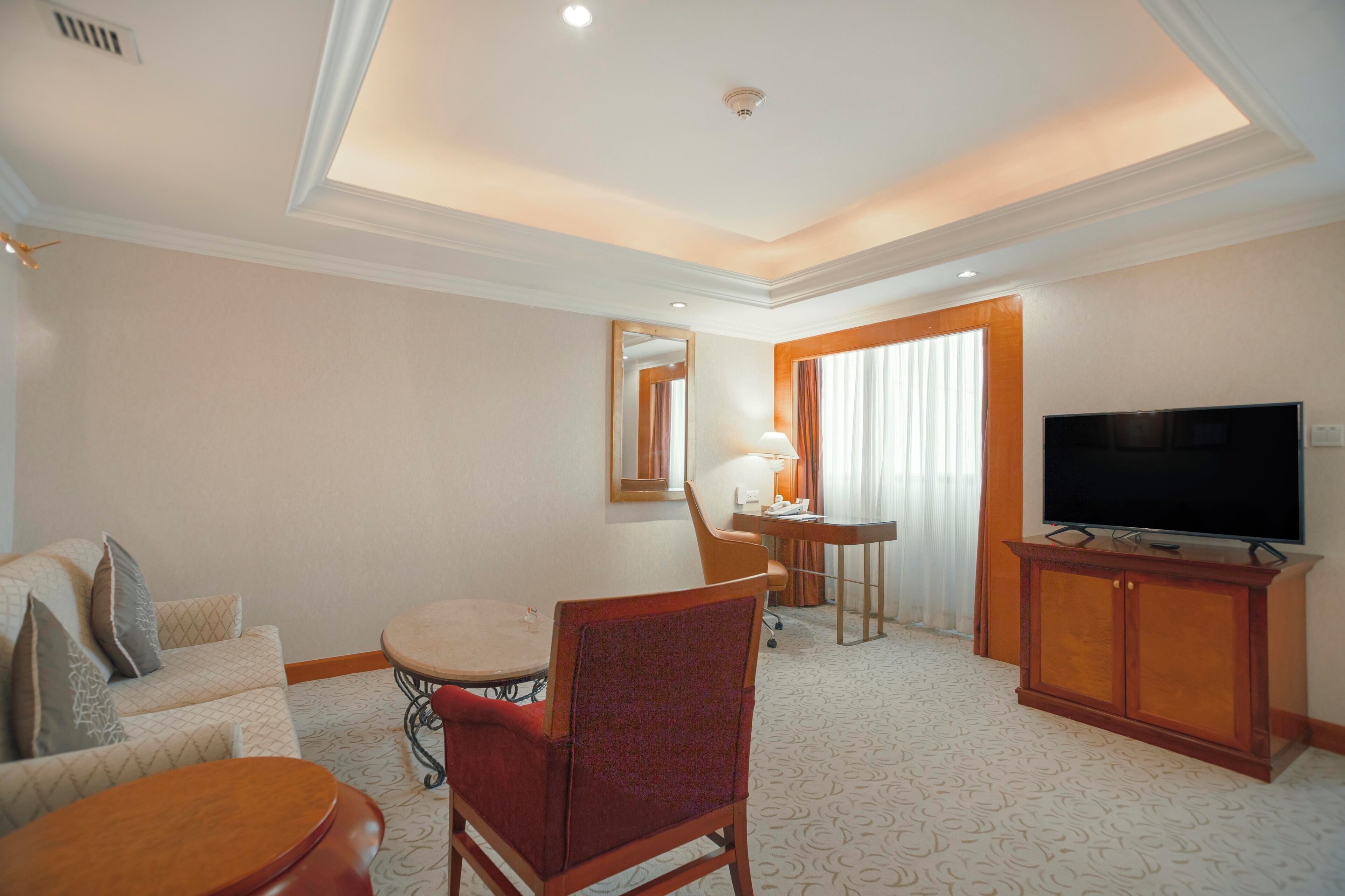 Een hotelkamer met een eettafel, een bank, een televisie en een spiegel.