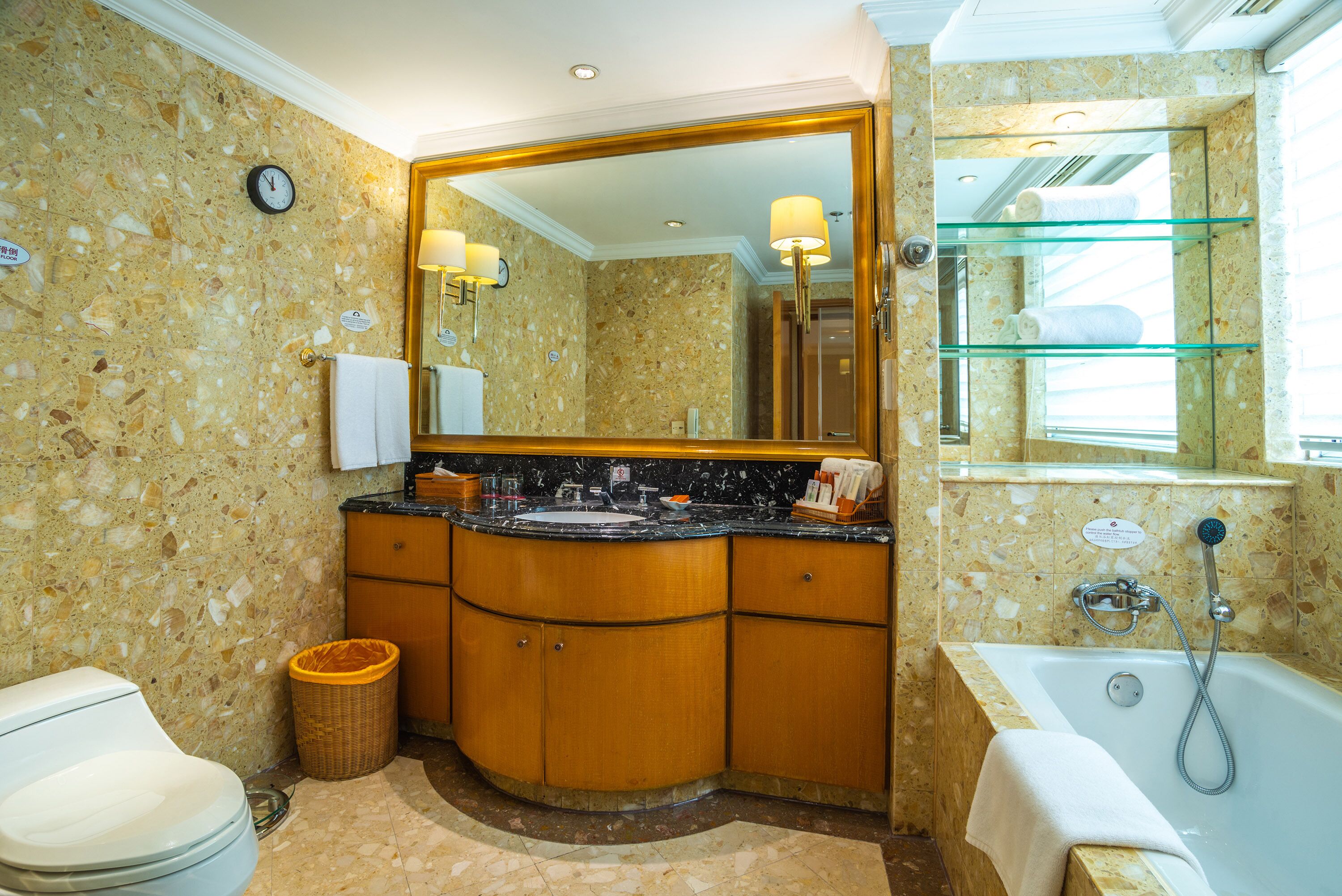 A bathroom with a marble wall, a large mirror, a sink, a toilet, and a bathtub.