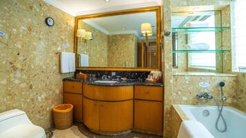 A bathroom with a marble wall, a large mirror, a sink, a toilet, and a bathtub.