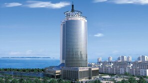 Een hoog, cilindervormig gebouw met een glazen gevel en een bord met de tekst 'Crowne Plaza' bovenop.