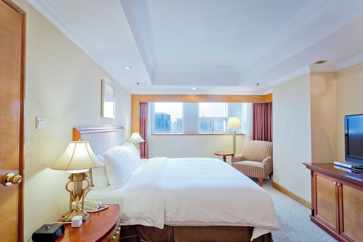 Een hotelkamer met een groot bed, nachtkastjes, een televisie en uitzicht op de stad.