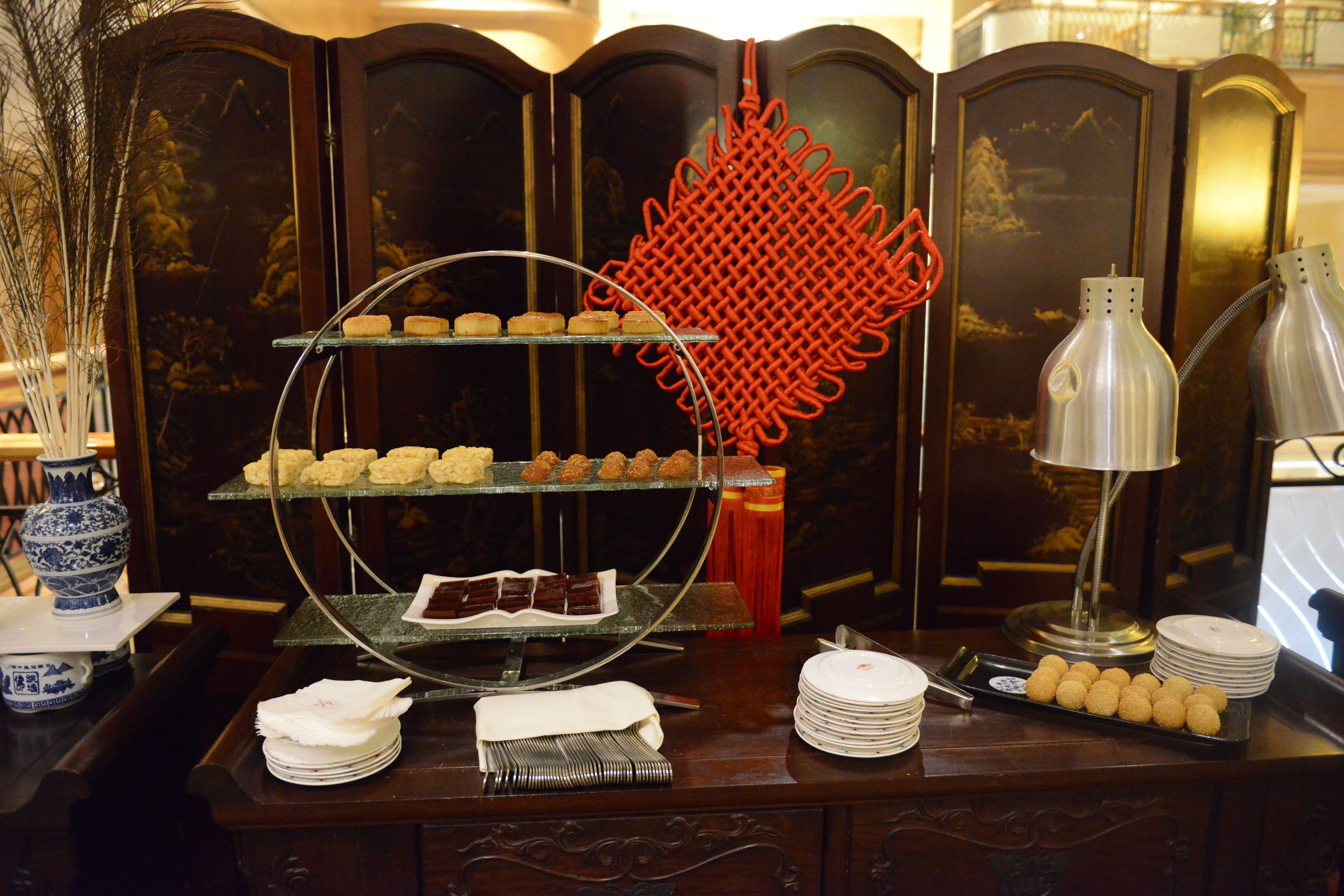 A buffet setup with multiple serving platters, a decorative red item, and a lamp.