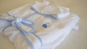 A neatly folded white towel with a blue ribbon and a small embroidered design, placed on a white surface.
