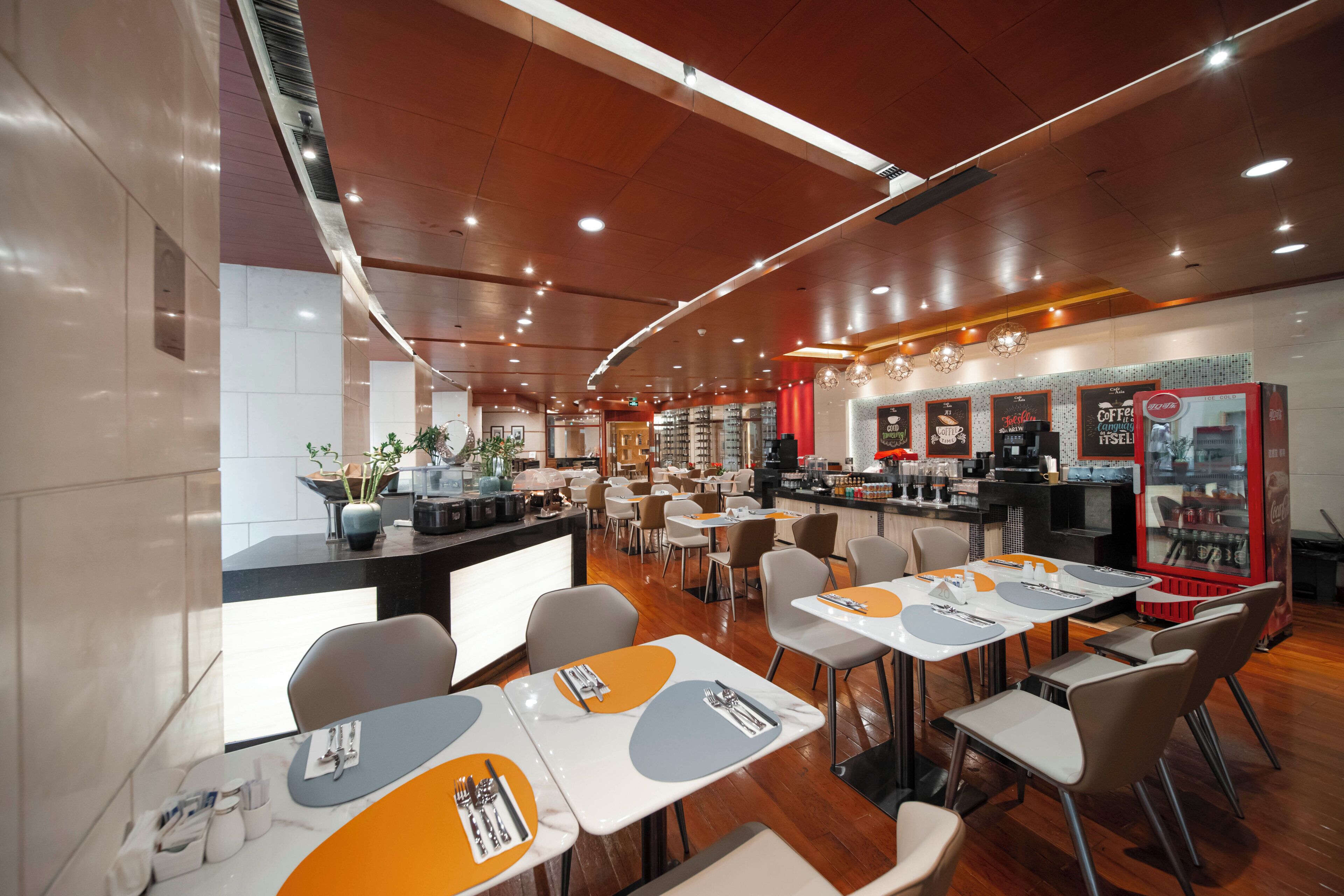 A modern restaurant with a curved ceiling, wooden flooring, and a counter with a coffee machine. Tables are arranged for dining with chairs.