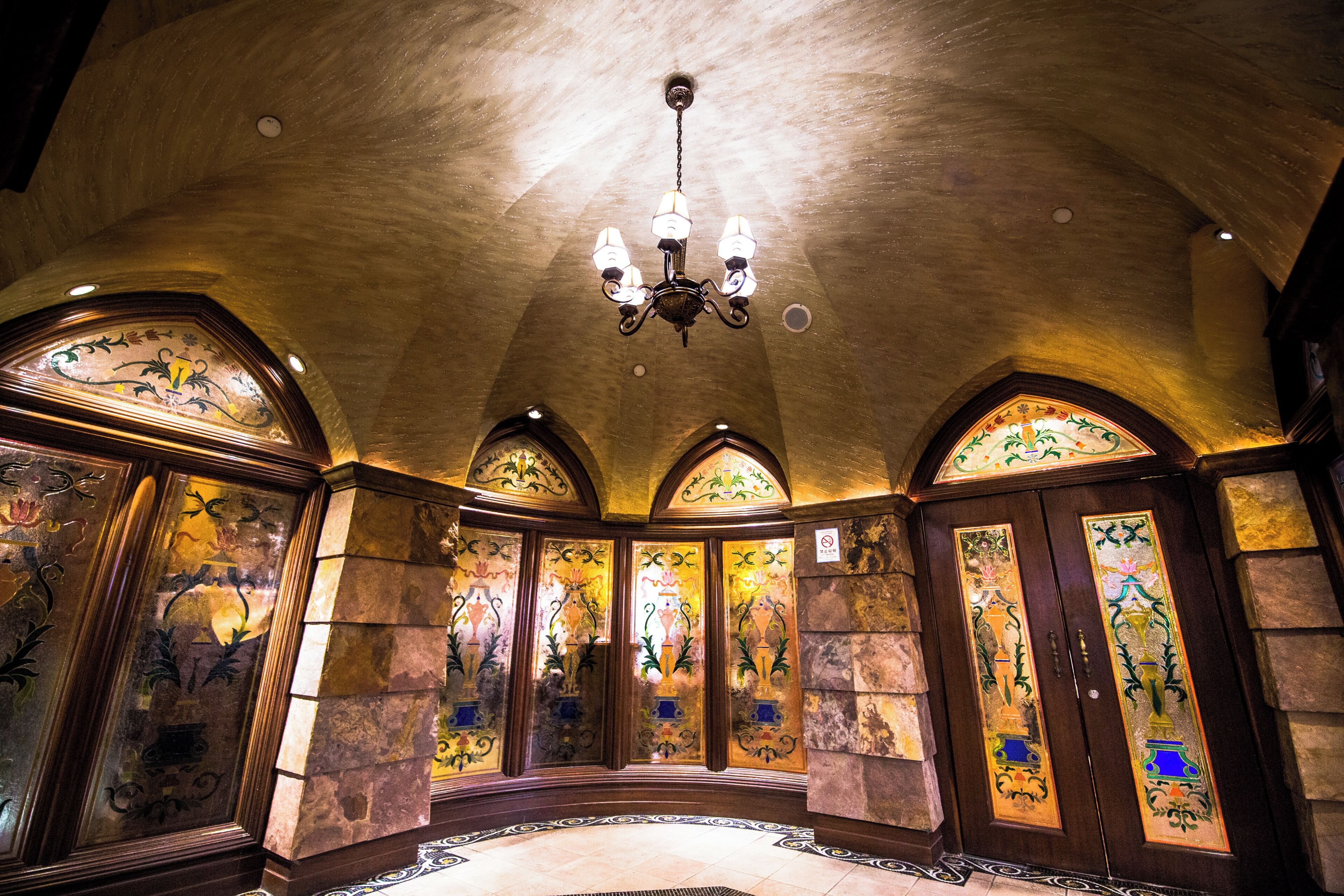 A grand hall with a high ceiling, ornate stained glass windows, and a chandelier.