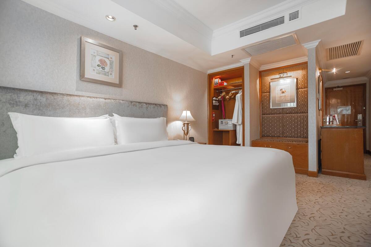 Een hotelkamer met een groot bed, een kledingkast, een spiegel en een ingelijste foto aan de muur.