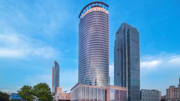 Un moderno edificio de gran altura con fachada curva, rodeado de otros edificios altos y un cielo despejado.